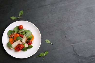 Delicious salad with chicken, vegetables and spinach on black table, flat lay. Space for text