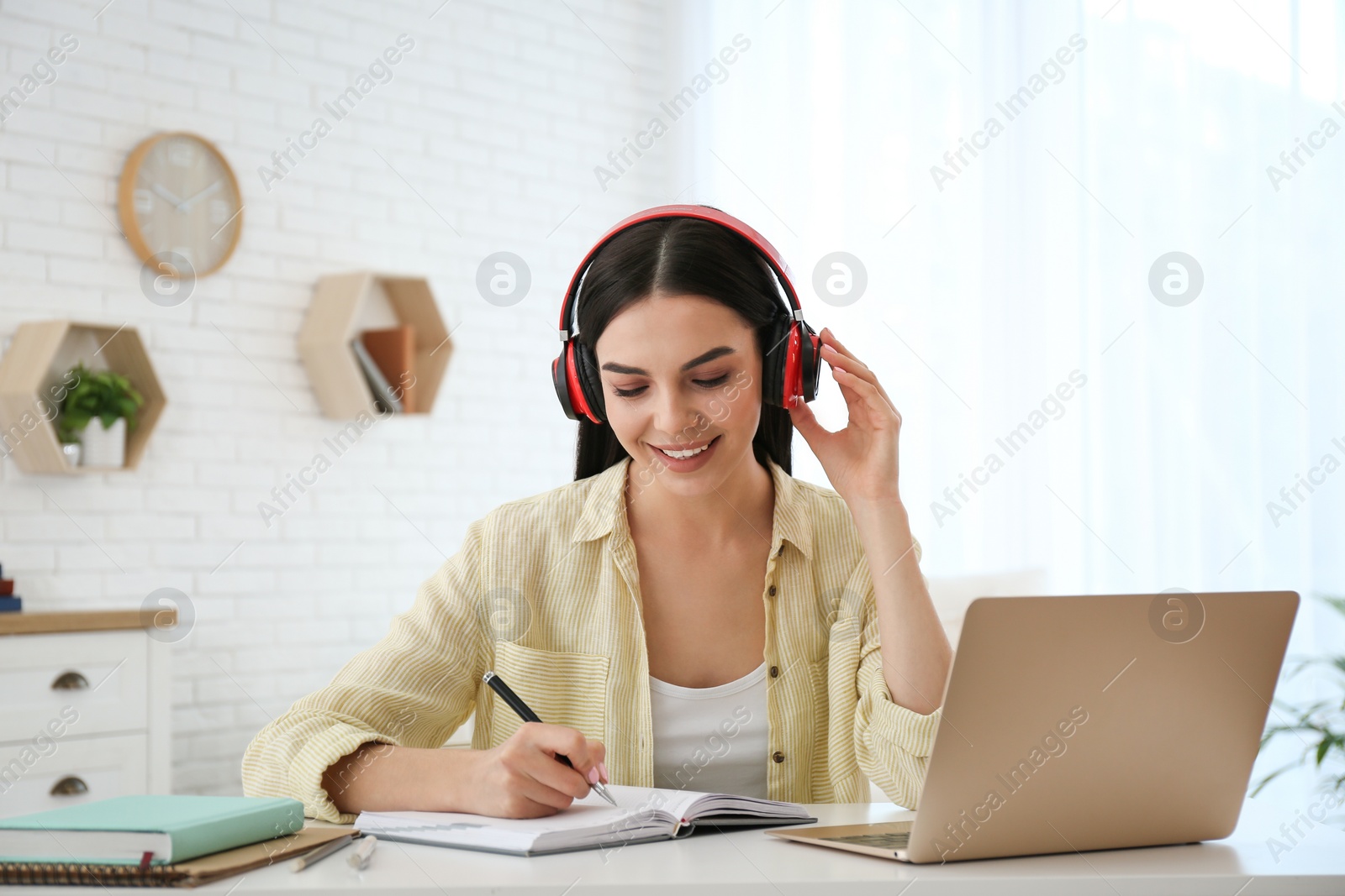 Photo of Young woman taking notes during online webinar at table indoors