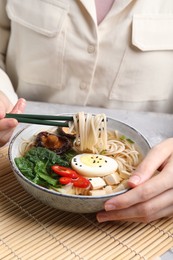 Photo of Woman eating delicious ramen with chopsticks at table, closeup. Noodle soup