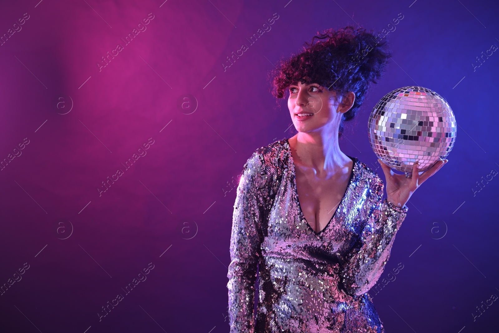 Photo of Beautiful young woman with disco ball posing on color background in neon lights. Space for text