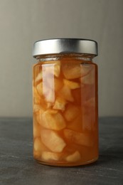 Photo of Tasty apple jam in glass jar on grey table