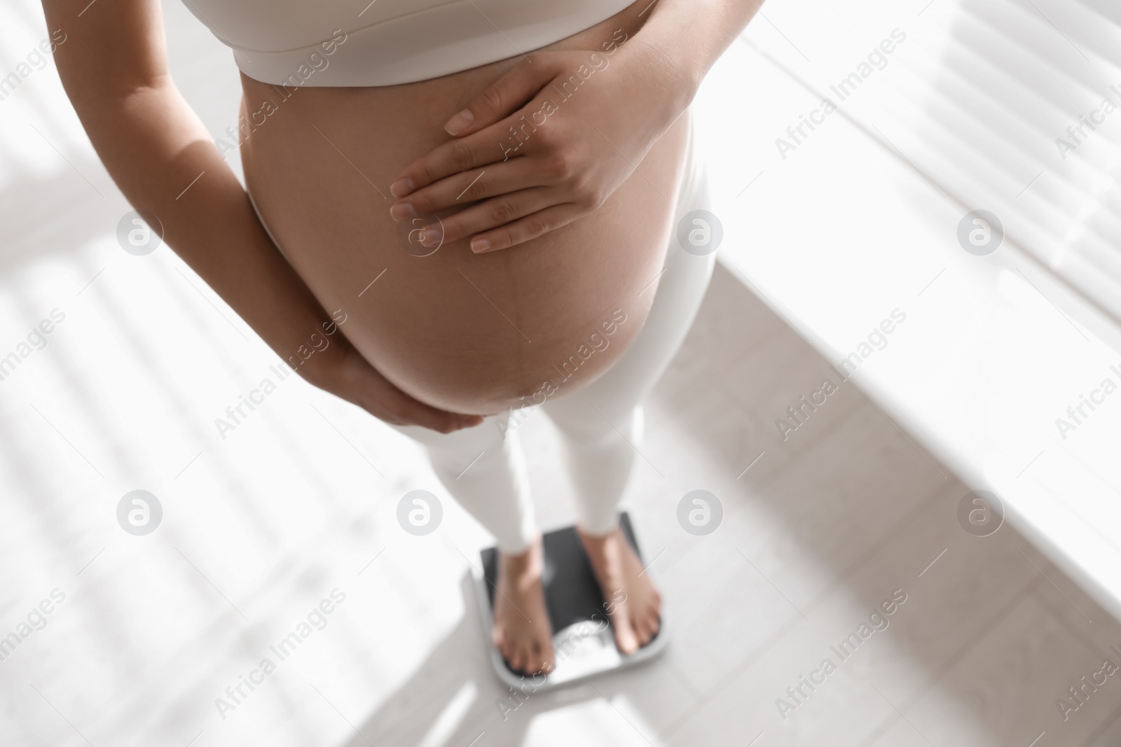 Photo of Pregnant woman standing on scales indoors, closeup