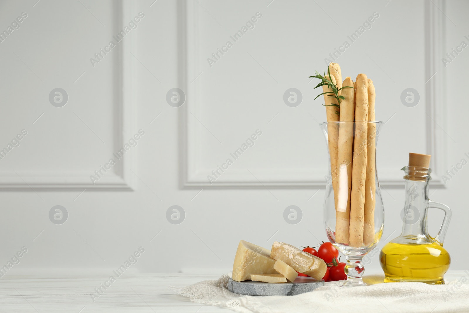 Photo of Tasty grissini with oil, tomatoes and cheese on white wooden table, space for text