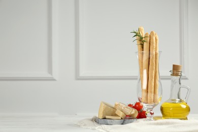 Tasty grissini with oil, tomatoes and cheese on white wooden table, space for text