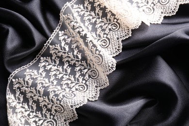 Photo of Beautiful white lace on black fabric, top view