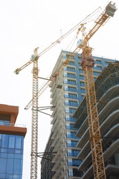 Photo of Construction site with tower cranes near unfinished building, low angle view