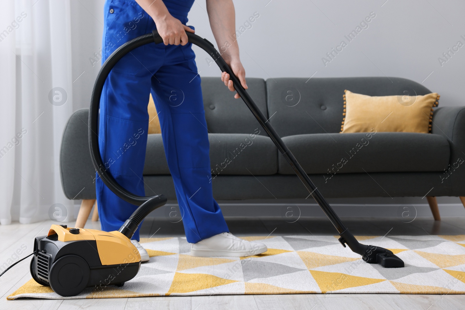 Photo of Dry cleaner's employee hoovering carpet with vacuum cleaner in room, closeup