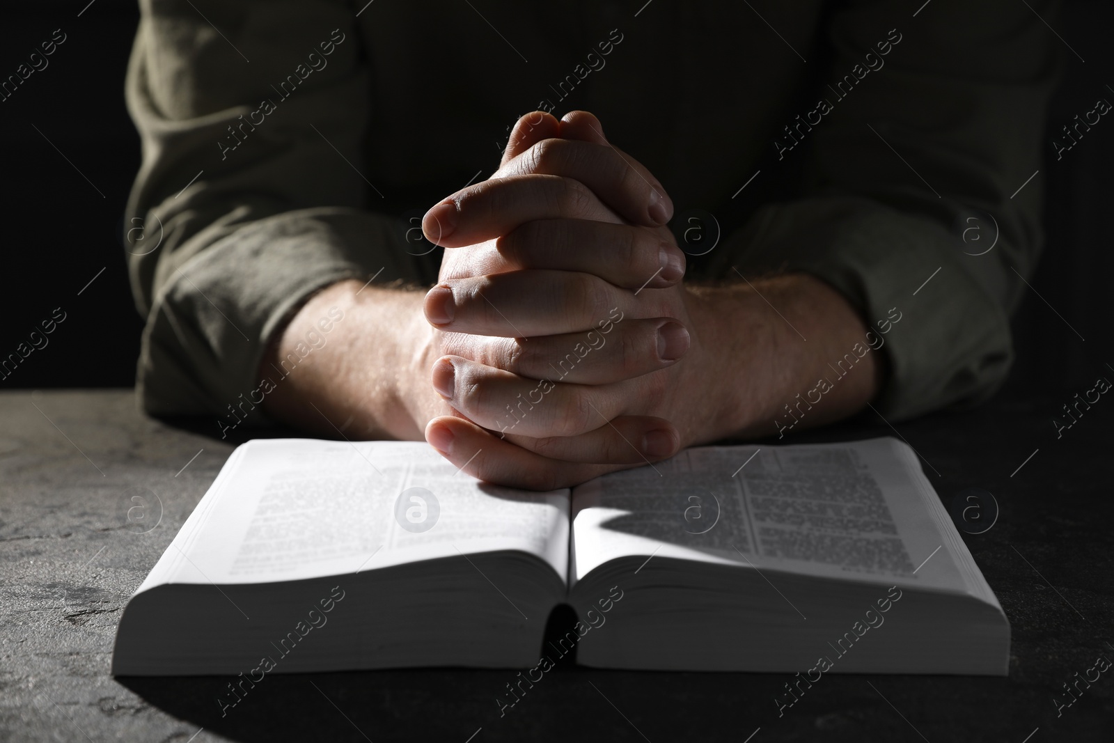 Photo of Religion. Christian man praying over Bible at table, closeup