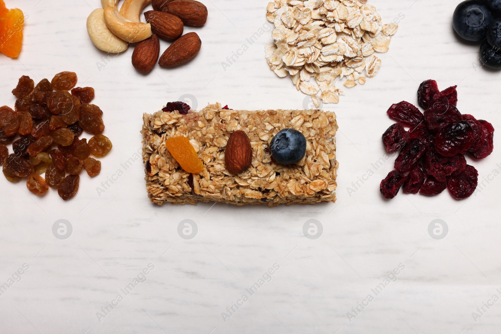 Photo of Tasty granola bar and ingredients on white wooden table, flat lay. Space for text