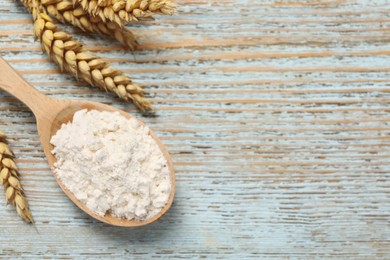 Spoon of wheat flour on light wooden table, flat lay. Space for text