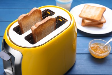 Photo of Yellow toaster with roasted bread and jam on blue wooden table, closeup
