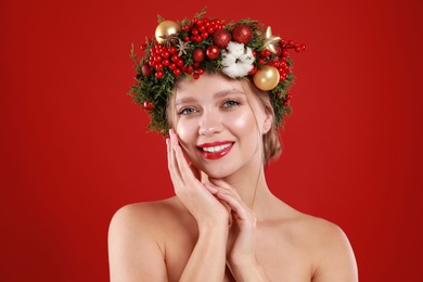 Beautiful young woman wearing Christmas wreath on red background