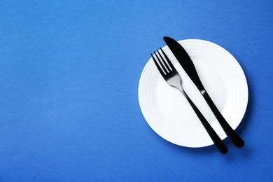 Photo of Clean white plate with cutlery on blue background, top view. Space for text