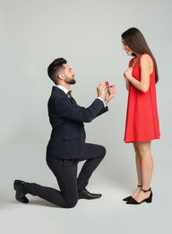Photo of Man with engagement ring making marriage proposal to girlfriend on light grey background