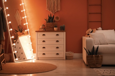 Large mirror with light bulbs and chest of drawers in stylish room interior