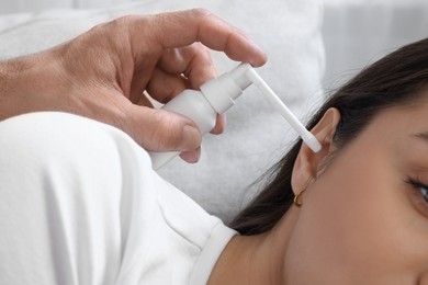 Senior man spraying medication into woman's ear on sofa, closeup