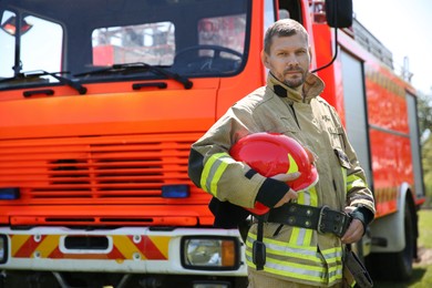 Portrait of firefighter in uniform with helmet near fire truck outdoors