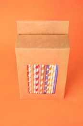 Photo of Box with many paper drinking straws on orange background