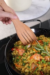 Woman cooking tasty rice with shrimps and vegetables on induction stove, closeup