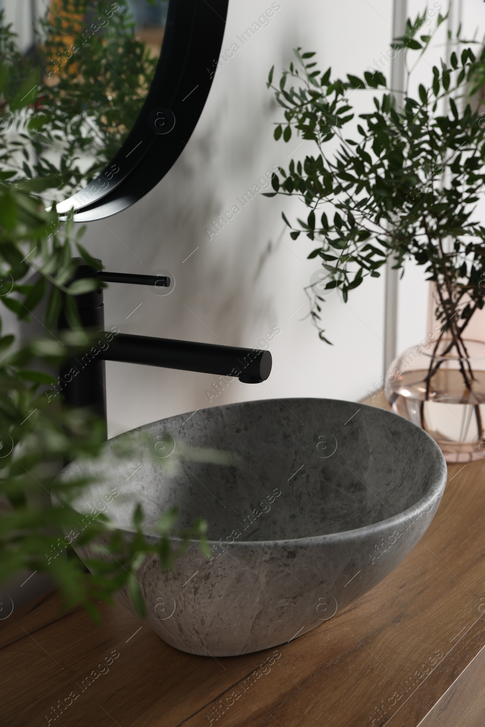 Photo of Eucalyptus branches near vessel sink on bathroom vanity. Interior design