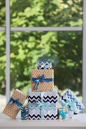 Many beautifully wrapped gift boxes on white table  near window. Space for text