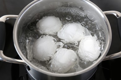 Photo of Chicken eggs boiling in pot on electric stove, closeup