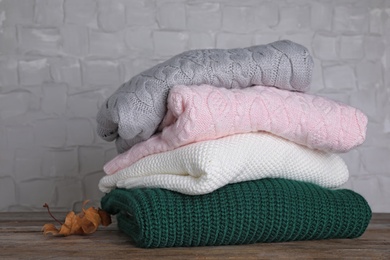 Photo of Stack of folded knitted sweaters and autumn leaf on wooden table against white textured wall