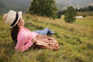 Young woman with backpack resting on green grass outdoors. Space for text