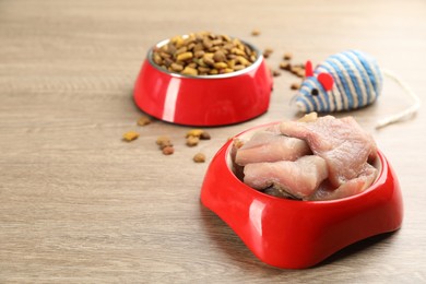 Natural pet food in feeding bowls and toy on wooden table, closeup. Space for text