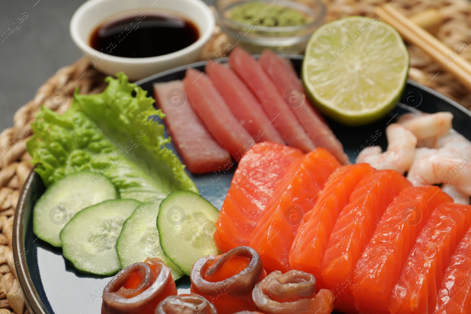 Photo of Tasty salmon slices, shrimp, cucumber and tuna on wicker mat, closeup. Delicious sashimi set