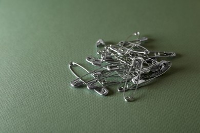 Photo of Pile of safety pins on green background, space for text