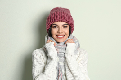 Young woman wearing warm sweater, scarf and hat on light background. Winter season