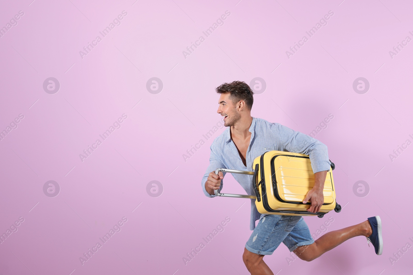 Photo of Young man running with suitcase on color background. Space for text