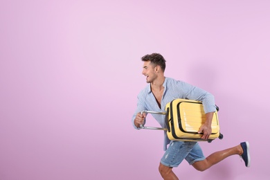 Young man running with suitcase on color background. Space for text