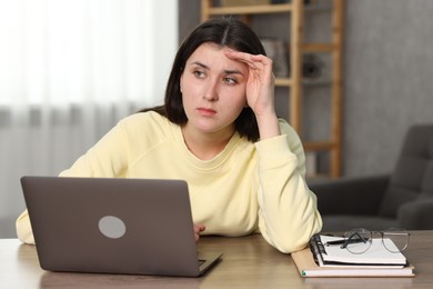 Overwhelmed woman sitting with laptop at table indoors