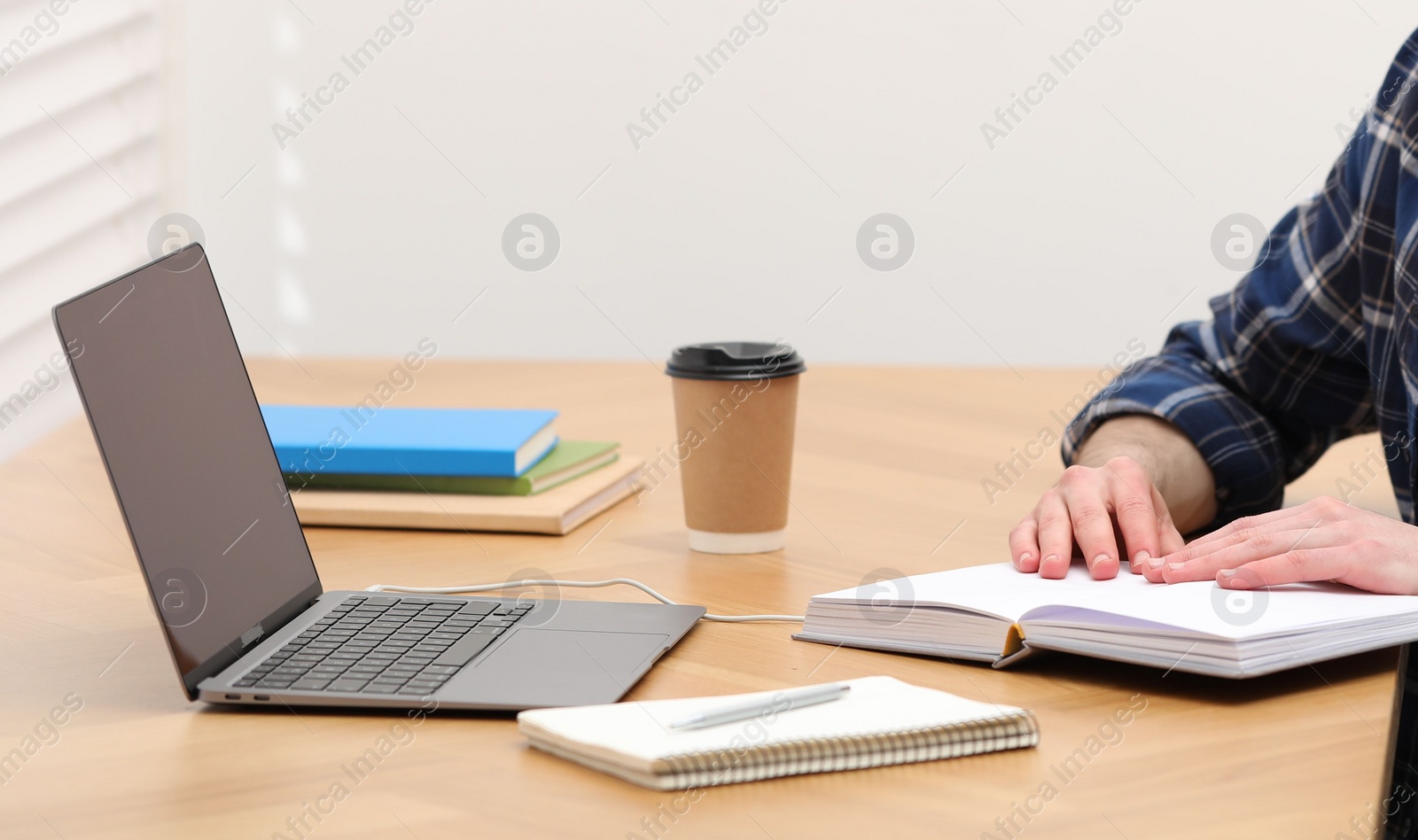 Photo of E-learning. Man taking notes during online lesson on table indoors, closeup