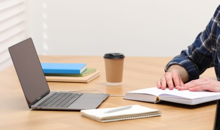 E-learning. Man taking notes during online lesson on table indoors, closeup