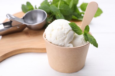 Photo of Delicious vanilla ice cream and mint in paper cup on white wooden table, closeup