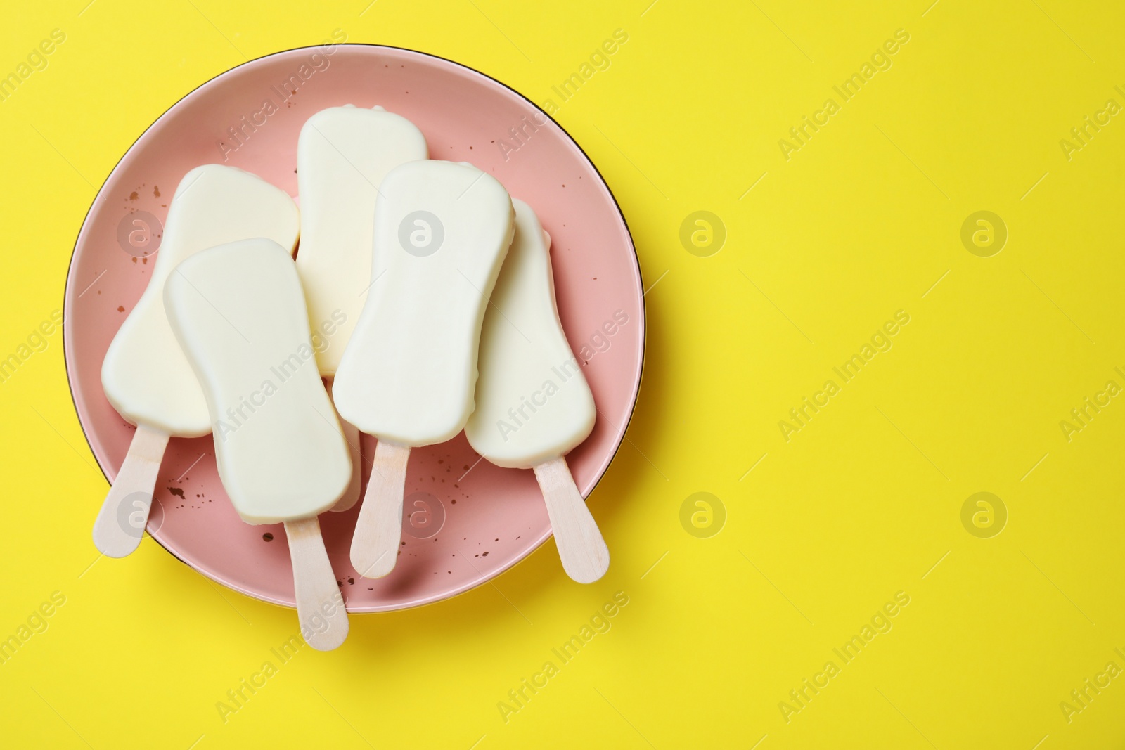 Photo of Plate with glazed ice cream bars on yellow background, top view. Space for text