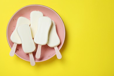 Plate with glazed ice cream bars on yellow background, top view. Space for text