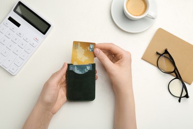 Woman holding leather card holder with credit cards at white table, top view