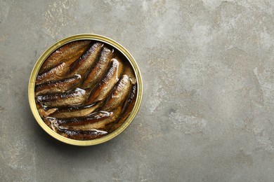 Photo of Sprats in tin can on grey textured table, top view. Space for text