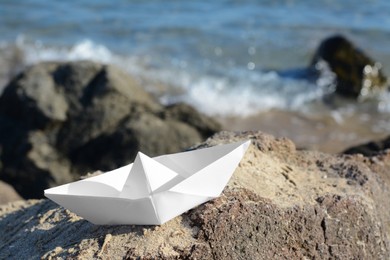 Photo of White paper boat on rock near sea, space for text