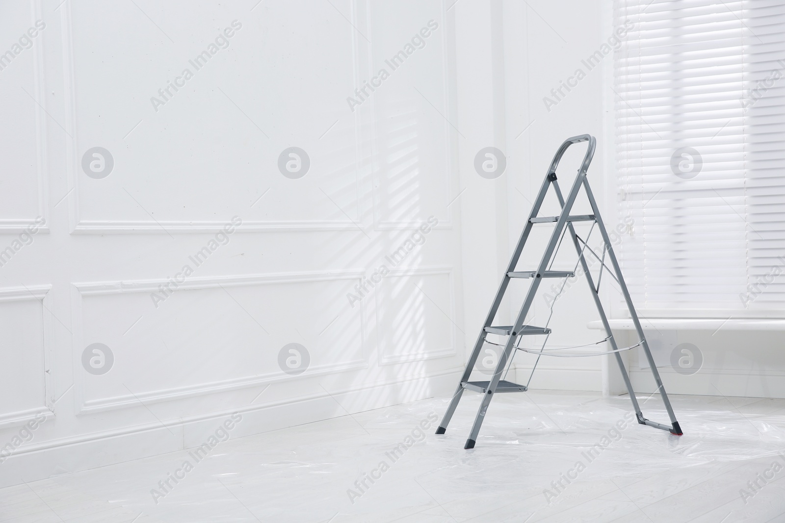 Photo of Metal stepladder on floor covered with plastic in empty room, space for text