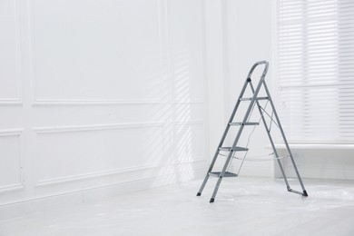 Photo of Metal stepladder on floor covered with plastic in empty room, space for text
