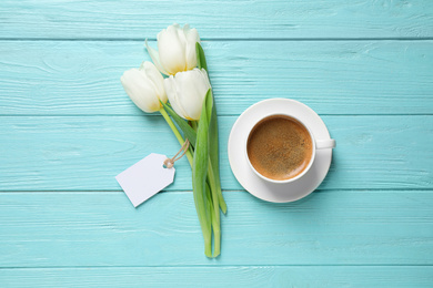 Photo of White tulips, coffee and blank tag on light blue wooden table, flat lay with space for text. Good morning