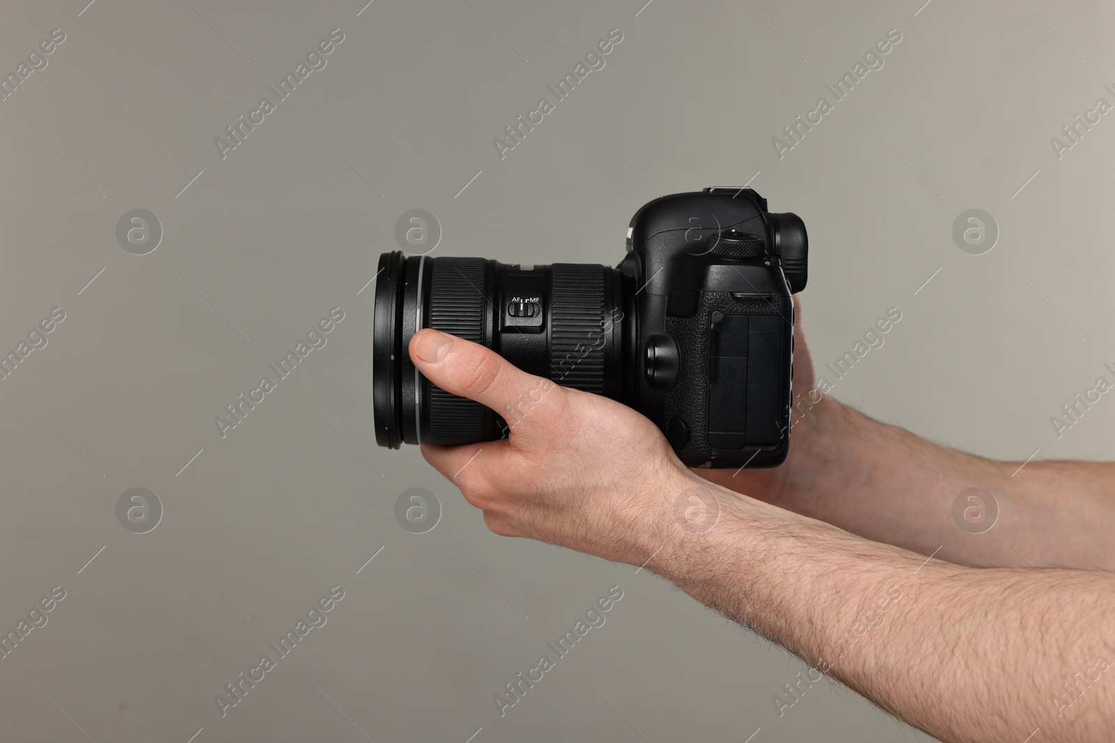 Photo of Photographer holding camera on grey background, closeup. Space for text