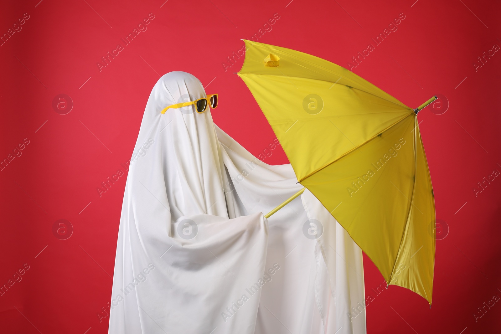 Photo of Person in ghost costume and sunglasses holding yellow umbrella on red background