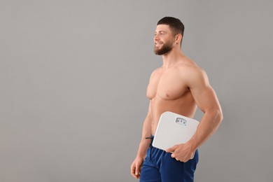 Happy athletic man holding scales on grey background, space for text. Weight loss concept