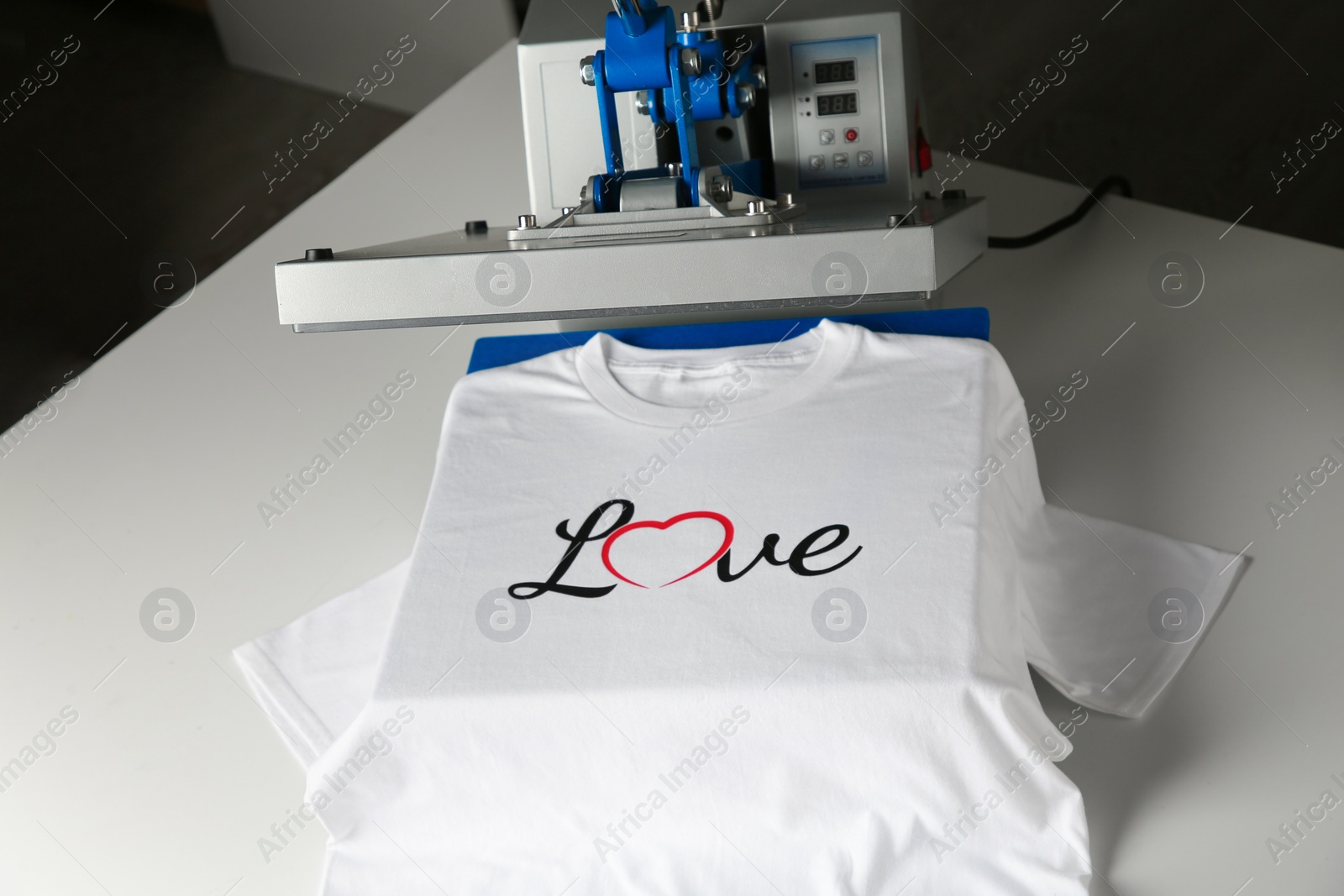 Photo of Printing logo. Heat press with t-shirt on white table